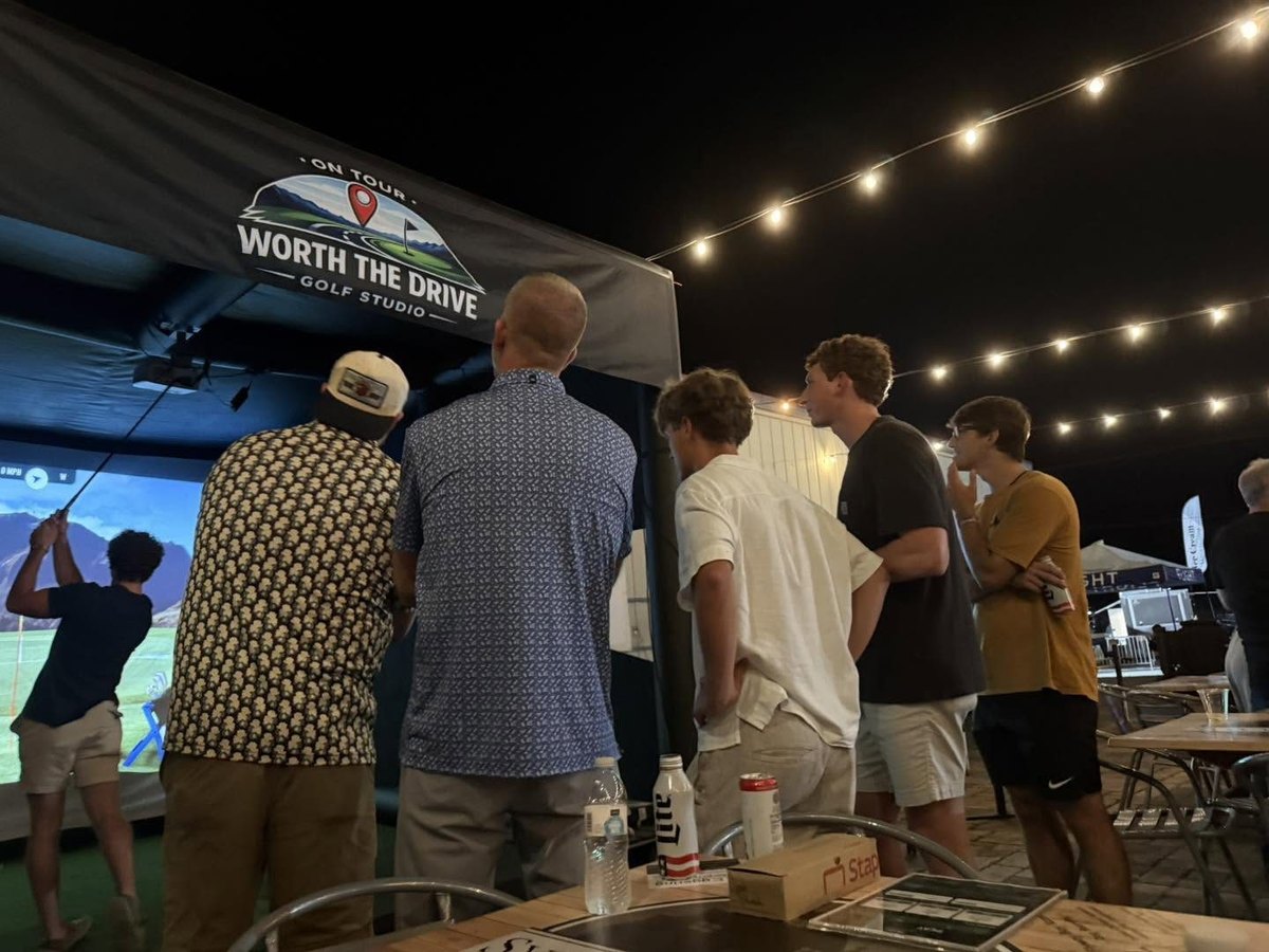 Guests watching a golfer play the mobile simulator under string lights at an evening event