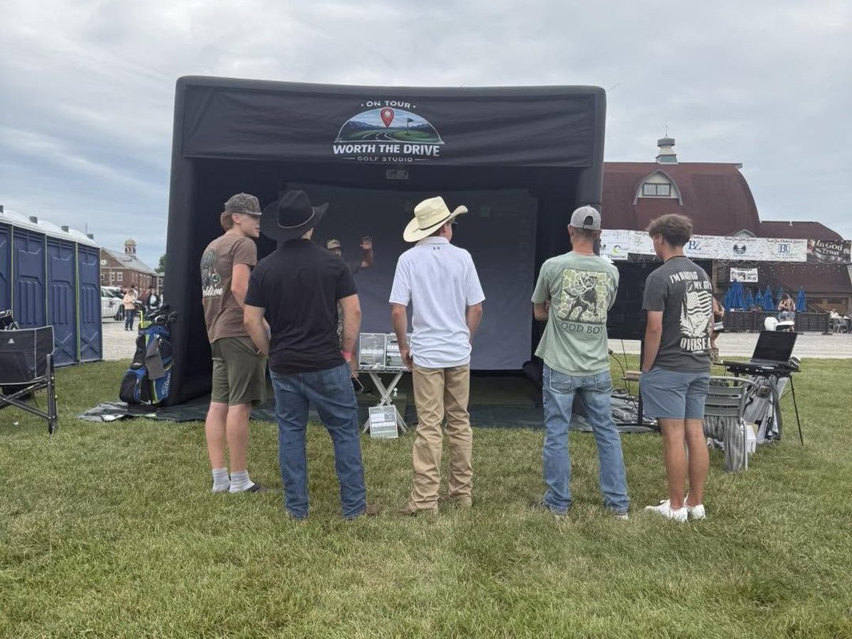 The mobile simulator set up outdoors on a grass lot with a group waiting to play