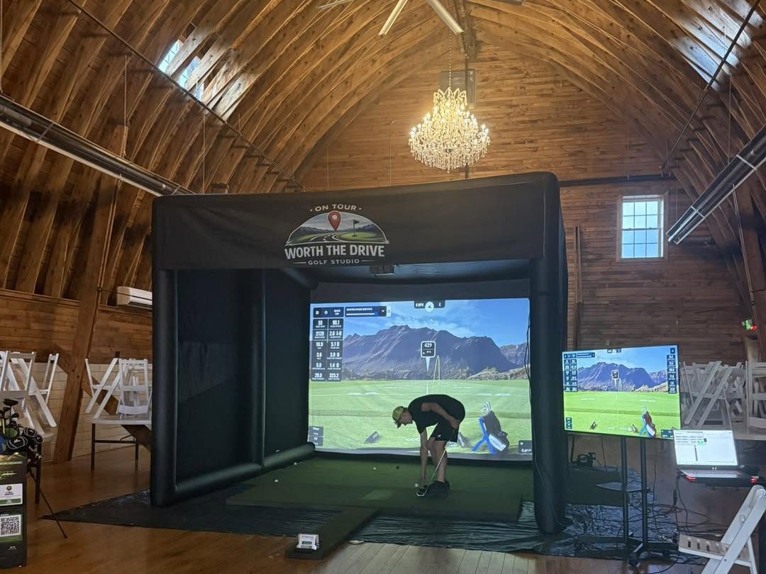The Worth the Drive mobile simulator set up under the chandeliers of a barn venue, a golfer mid-swing